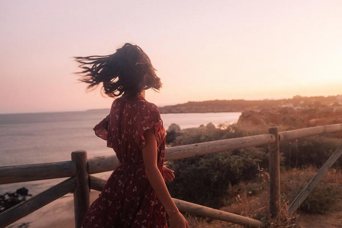 Mimi in a red dress, hair in the wind, on a cliff above the sea at sunset
