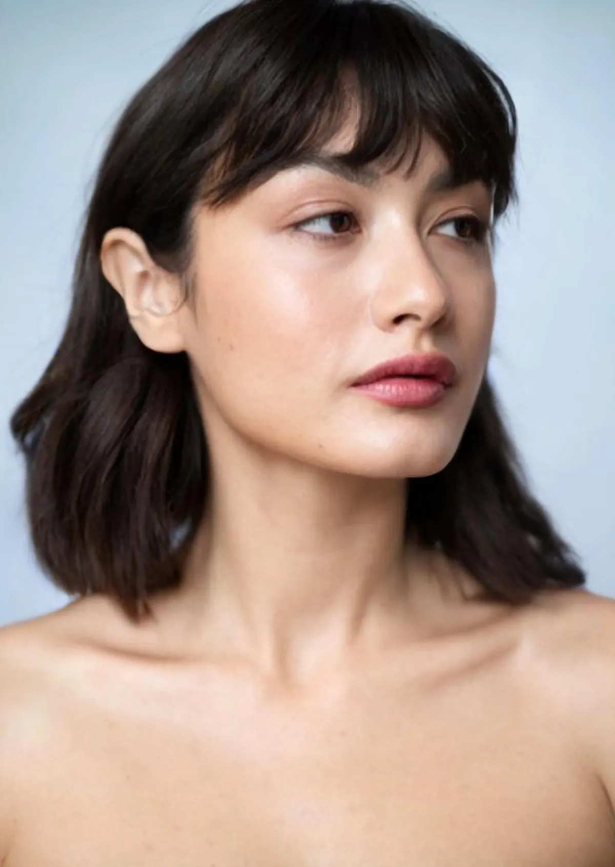 Portrait of Mimi with a dark fringe against a pale blue background